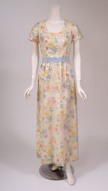 This Richard Kaplan, New York dress is so feminine. The white Dotted Swiss fabric is printed with pastel Spring flowers. They are embellished with opalescent sequins and rhinestones.
The dress has a blue grosgrain ribbon belt at the Empire
