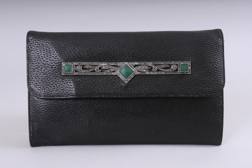 A black textured leather clutch from the Art Deco period is enhanced with a design of marcasites and three large green chrysoprase stones on the front. The interior of the fabric lined bag is divided into two sections with a slip pocket as well as a