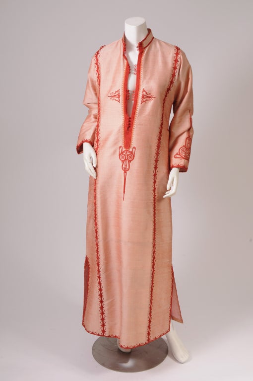 Pale coral colored hand woven silk is beautifully accented with a deeper coral colored soutache trim in this chic caftan deigned in Lebanon in the 1970's. The low cut neckline has clusters of buttons and loops so that it can be closed up or left