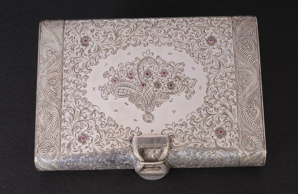 Continental silver is highly chased and set with rubies to create a lovely evening bag from the 1930's or 40's. The clasp opens to reveal a large beveled mirror in the top, a pop up silver lipstick holder, and three chased silver compartments for