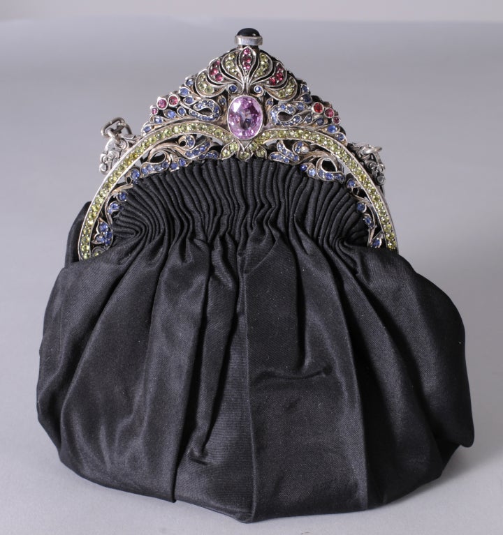 This stunning bag has a pierced silver frame set with pastel tone prong set jewels including pink and blue sapphires and green peridot. The back is pierced and chiseled in the same design. the gathered black satin bag has an envelope-shaped change