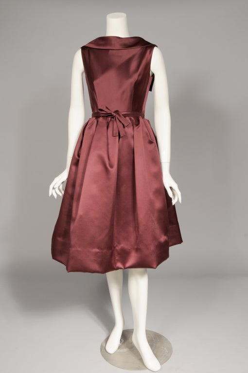 A stunning burgundy wine colored silk is the perfect choice for this elegant cocktail or dinner dress designed by Norman Norell
in the 1960's. The sleeveless dress has a rolled collar in front which dips low and wide in the back. There is a row of