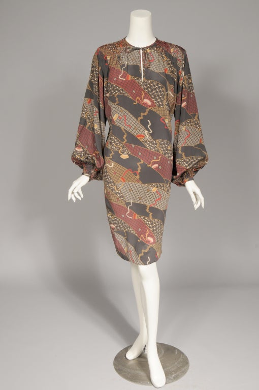 A lovely Oriental fan pattern is printed on a medium grey silk. The dress has a round weighted neckline with a self tie. The shoulders are smocked with red silk thread. The long full sleeves are also smocked just above the narrow one button cuff.