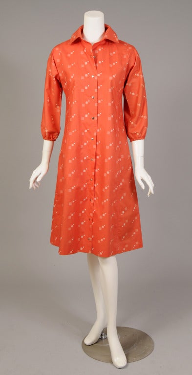 This easy to ear Marimekko cotton dress is coral cotton with a pattern of white squares. The dress has snaps at the center front, elasticized sleeves and two pockets concealed in the seams. It is marked a vintage size 6 and it is in excellent