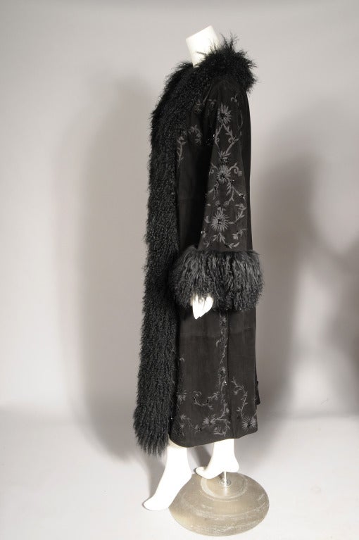 A very glamorous black suede coat designed by Adrienne Landau is lavishly embroidered and beaded in black on black. A generous amount of black Mongolian lamb edges the center front and cuffs. The coat has no closures, two pockets are concealed in