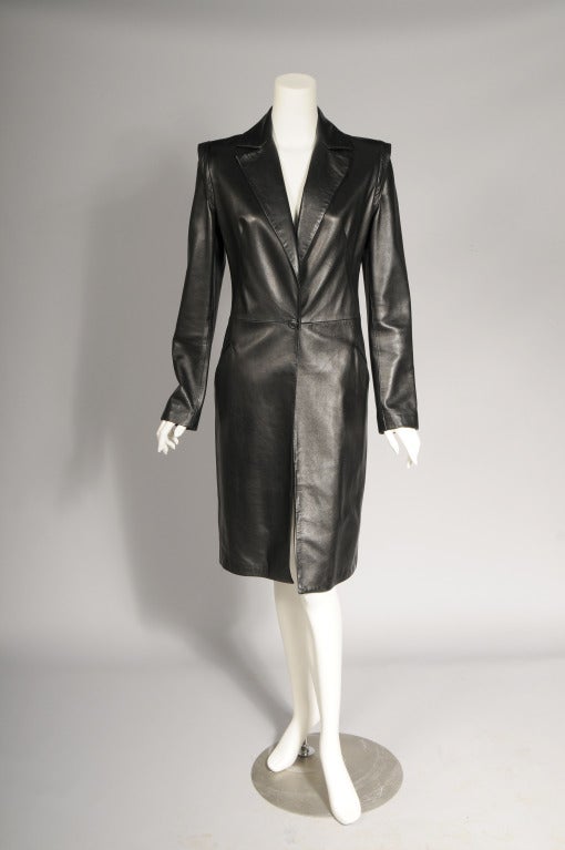 Supple black leather lends an air of elegance to this coat designed by Gianni Versace in the 1990's. There is an interesting shoulder treatment  and a single button closure at the waist. The coat is fully lined with a Medusa head woven fabric. It is