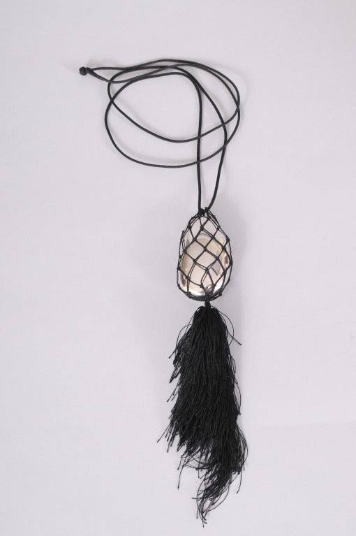 An unusual form for the iconic Elsa Peretti bean, this large sterling silver bean is cradled in a woven mesh bag. A large black tassel is suspended from the bag and a black cord completes the necklace. It is in excellent
