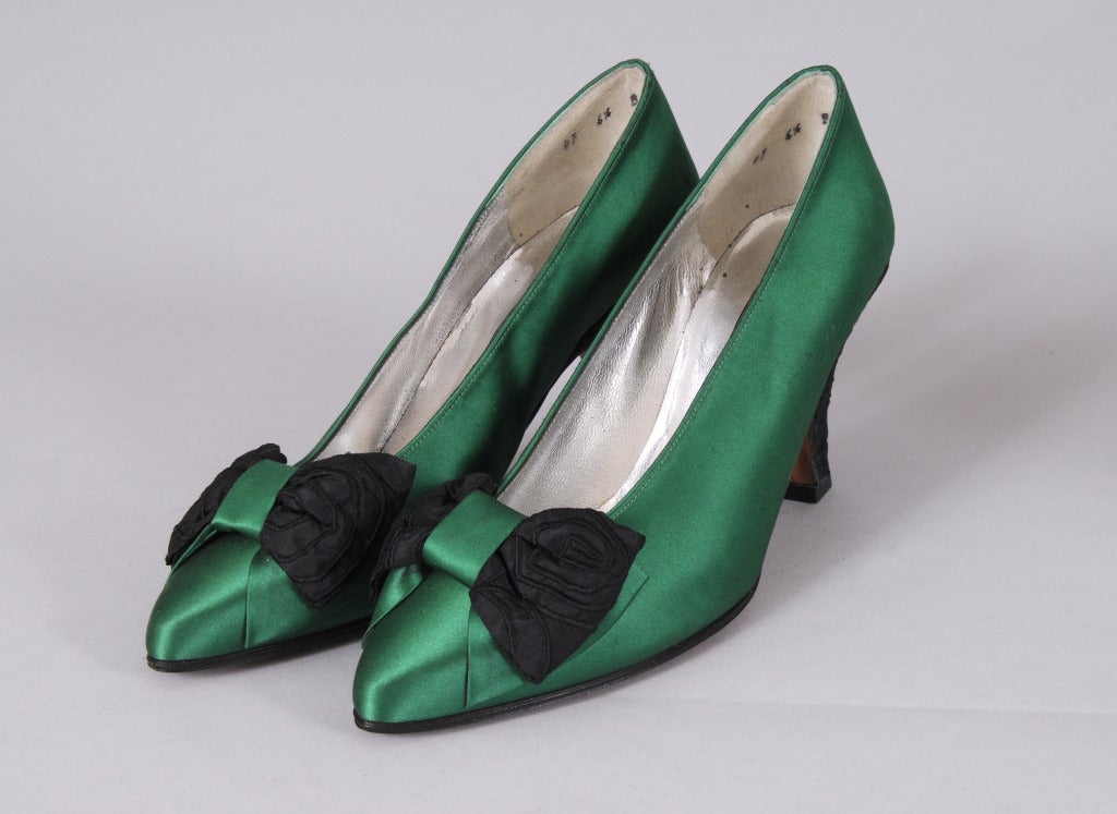 Emerald green satin shoes are accented with black woven silk bows and heels. Lined in silver kidskin they are in excellent condition and marked a size 6 1/2.