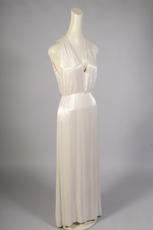 This spare and elegant ivory silk dress designed by James Galanos is completely hand beaded in sparkling ivory bugle beads. The bodice has a deep V neckline and is open to the waist in back. The bugle beads are sewn on an angle allowing the dress to