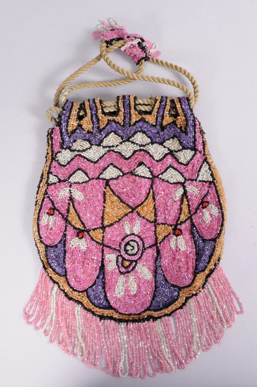 From a Beverly Hills collector, this sweet Art Deco beaded  bag  combines bright pink beads with mauve, grey and gold beads with red accents and black outlines. The bag has a bead decorated drawstring top and a lush pink and grey beaded fringe at