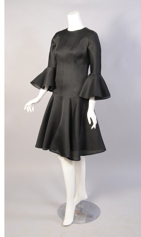 Chic et élégante, cette petite robe de cocktail en gazar de soie noire, signée Cristobal Balenciaga, est totalement intemporelle. La robe a un décolleté rond, des manches longues avec de profonds volants, un col tombant.  et une jupe ample sur une
