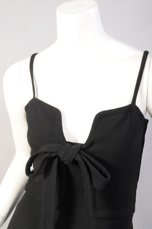 A figure flattering low neckline, accented with a softly tied bow, defines this slim black wool dress designed by James Galanos in the 1970's. The dress has narrow straps, a left side zipper and it is fully lined in black silk. Retailed by Saks