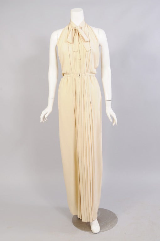 Creamy silk crepe is pleated from the collar to the hemline in this halter dress designed by James Galanos in the 1970's. The collar ties above three buttons at the center front. The waist is elasticized and there is a zipper at the center front of