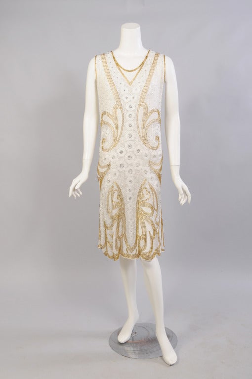 A striking, larger sized, French hand beaded Flapper dress from the 1920's is almost completely covered with gold, silver, crystal and white beads. The dress is white cotton, gauranteeing that it is sturdy and can definitely be worn many more times.