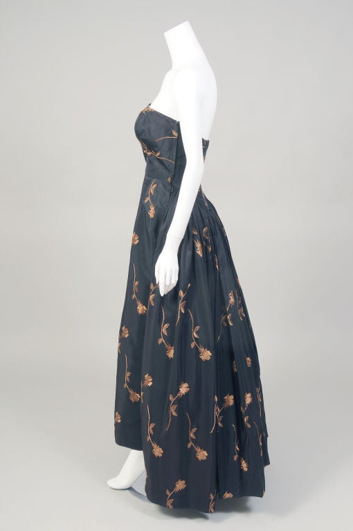 Fitted and full, sexy and demure, black and floral, this amazing strapless ballgown from the 1950's seems to capture the contradictions in a changing society quite fashionably.<br />
The fitted bodice is boned for support and it sits at the natural