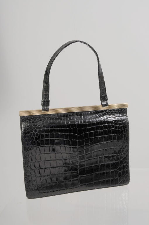 Retailed by Cartier, London this striking black crocodile bag has a 9K gold ribbed frame.  The frame is marked on the back side of the bag.  The bag can be carried as a clutch or by the narrow crocodile swing strap.  There are two snaps at the