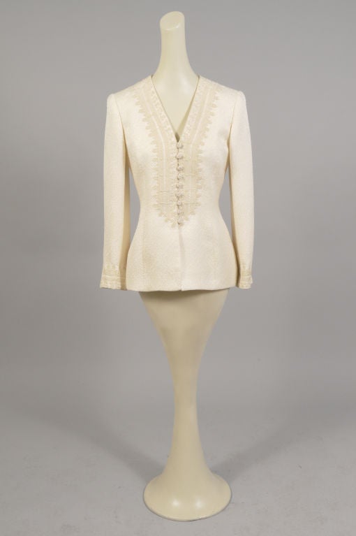 A textured woven cream colored silk is trimmed with Moroccan inspired golden soutache braid in this elegant jacket from Oscar de la Renta.<br />
The jacket has two snaps and a series of braid covered buttons and loops at the center front. The