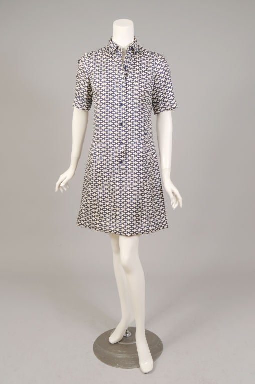 A simple sheath, in a classic Hermes logo print in their sumptuous silk, is done in a navy and cream colorway. The dress slips on over your head. It has a button down collar, short cuffed sleeves and a center front button placket opening to just