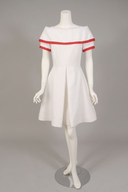 Crisp white waffle weave cotton pique is accented with bright red trim on the collar and sleeves in this dress from Arnold Scaasi. The dress has a wide, off the shoulder neckline, a generous collar, short sleeves and a fitted waist. The skirt has an
