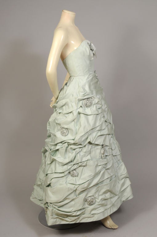 Pale cealdon green silk is lavished with bows and ribbon roses by Philip Hulitar for a truly unforgettable ballgown. The strapless dress has a fitted, boned bodice above a full ruched skirt. The intricately hand sewn skirt is gathered in waves,