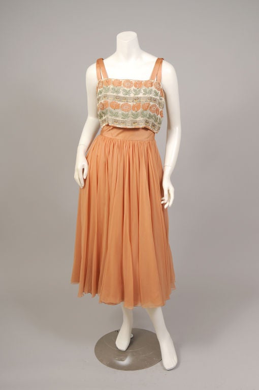 An amazing dress from the 1950's, designed with a woven floral patterned brocade bodice and a gorgeous silk chiffon dance skirt. The double straps and cummerbund are peach satin. The bodice closes with hooks and eyes at the left side, the cummerbund