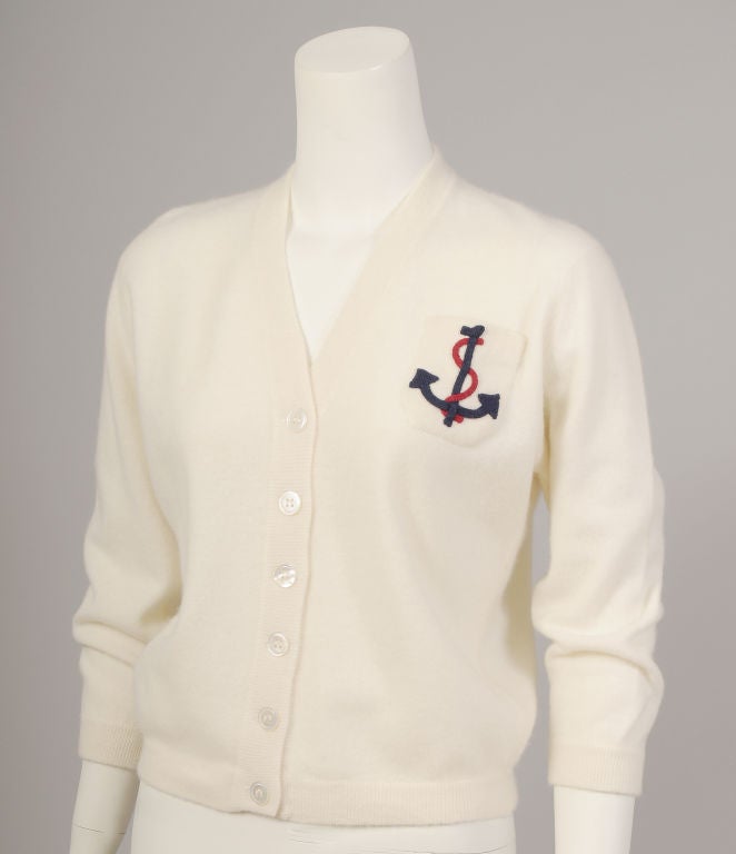 A cream colored cashmere sweater from Dalton, Scotland has a V neckline and a six button front closure. The breast pocket is embellished with a red and navy anchor insignia. The sweater is in pristine condition and appears