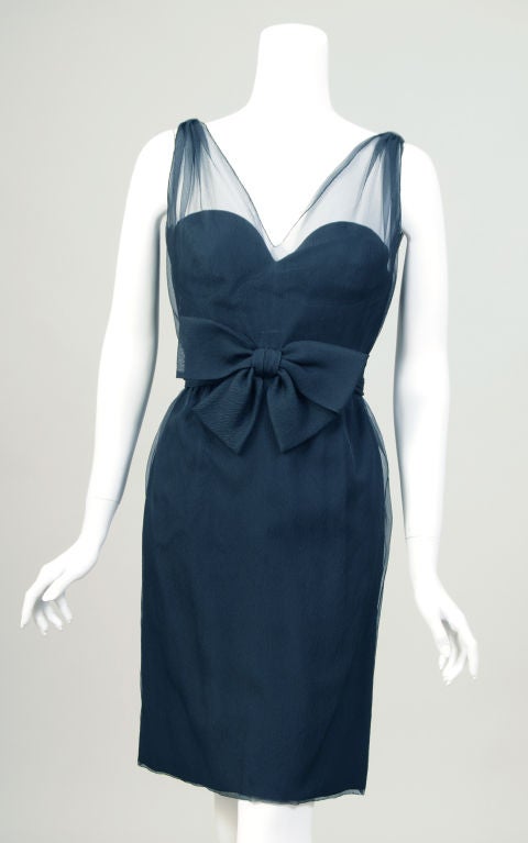 A black silk crepe strapless cocktail dress is fitted in all the right places. The dress has a sweetheart neckline and a bow at the waist. There is a sheer layer of black silk georgette which is gathered at the shoulders, as well as a wide