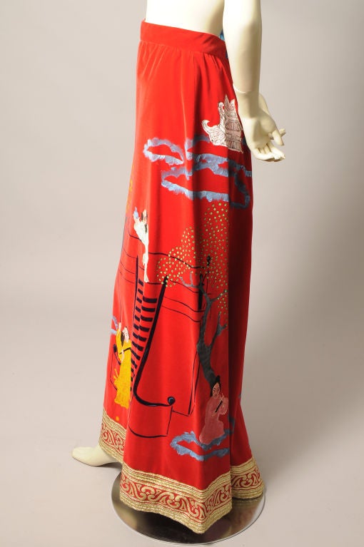 Red cotton velvet is the brilliant background for a charming hand painted Asaian scene encircling this long evening skirt. Chinese men and women are engaged in various activities in a lush landscape. The hemline is bordered by a wide woven gold
