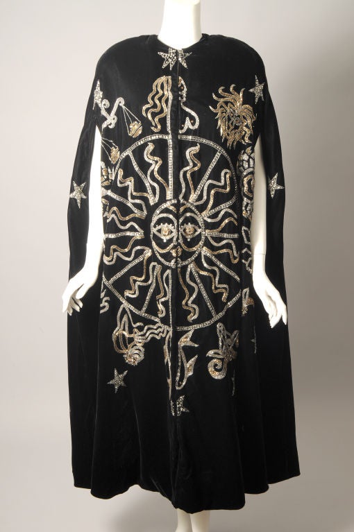 A striking beaded design is the focal point of this rich black velvet cape from Bob Mackie. The signs of the zodiac surround a bold and graphic sun. They are worked in silver and gold bugle beads, rhinestones and sequins. The cape is fully lined and