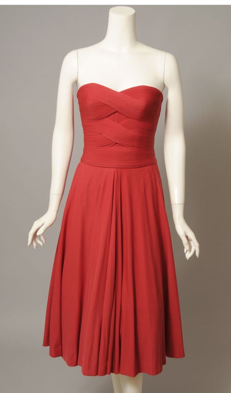 Madame Gres drapes cherry red silk jersey in her signature style on the bodice of this elegant short evening dress from the 1950's. The meticulously pleated fabric is draped and stitched to create the most flattering silhouette. The strapless dress