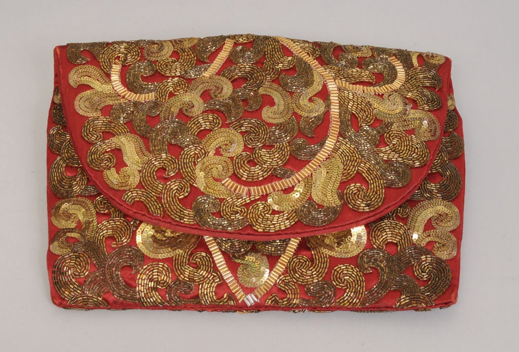 A red satin clutch bag is lavishly embellished with gold beadwork, creating the perfect accent for a LBD.<br />
The beads have a rich gold patina acquired over time. The bag has a large scale design of a leaf on a vine covering the front and the