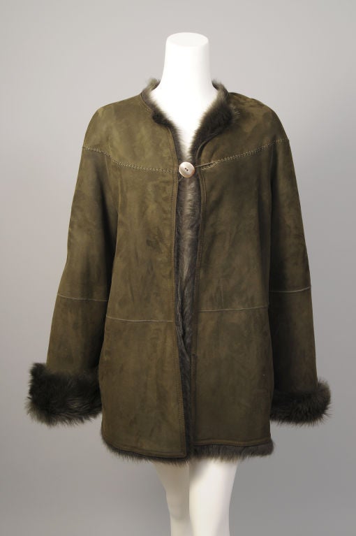 A fabulous, light weight lambskin shearling jacket from Bill Blass is done in a lovely deep green with a matching green fur interior. The collarless swing jacket has a decoratively cross stitched yoke with a lrage single button for the closure.