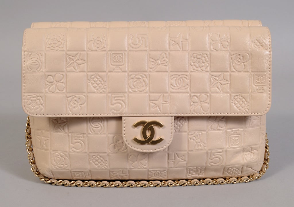 A pristine and unusual double sided Chanel bag is impressed with all of the iconic Chanel logos. The Number 5, a perfume bottle, a camellia and a heart with double C's are among the designs on the bag. The chain strap with leather trim, the