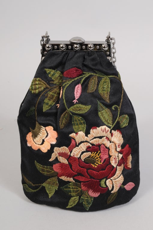 Beautiful floral embroidery decorates the front of this pristine black satin evening bag from Valentino. The bag has a flawless metal frame and an adjustable chain strap. It is fully lined in a woven silk and it comes with the original sleeper