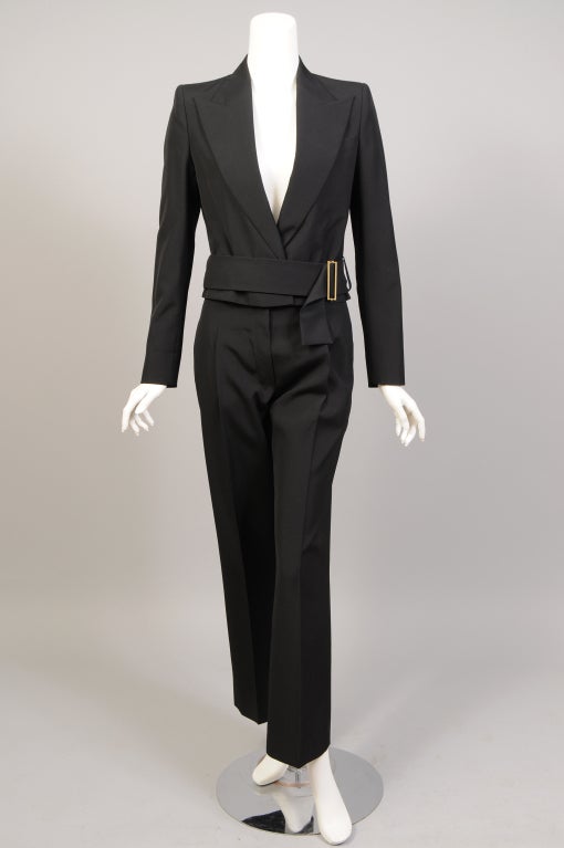 A contemporary classic, this light weight black wool jacket and pants from Yves Saint Laurent Rive Gauche is in pristine condition and appears to have never been worn. The cropped jacket has an attached belt that wraps and buckles. The sleeves have