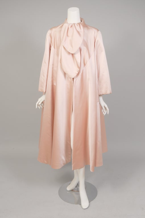 The most luscious shade of pale pink satin is used inside and out for this ultra feminine 1950's swing coat from Norman Norell designing for Traina-Norell.  The coat has an attached scarf that can be worn in a variety of ways. There is a satin