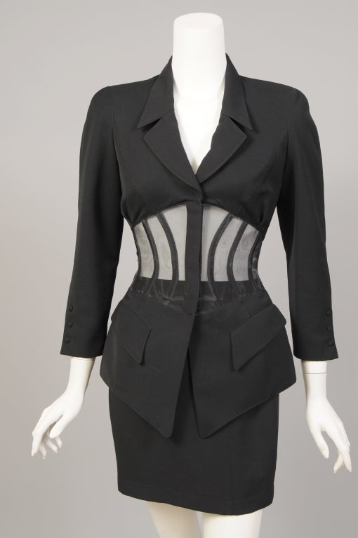 The ultimate 80's power suit is a Thierry Mugler corset suit.
This stunning jacket is tailored with notched lapels, hip pockets and a hidden zipper closure. The waistline is a boned corset of sheer black mesh. The matching mini skirt is fully lined