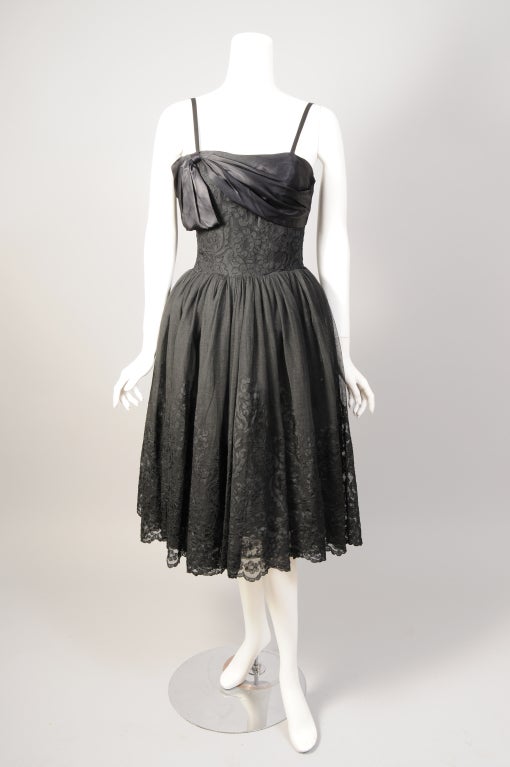 A Mainbocher black lace cocktail dress is the ultimate Little Black Dress. Designed in the 1950's after his return from Paris during World War II, this dress is so feminine. The front of the bodice is wrapped in black satin above black lace. The
