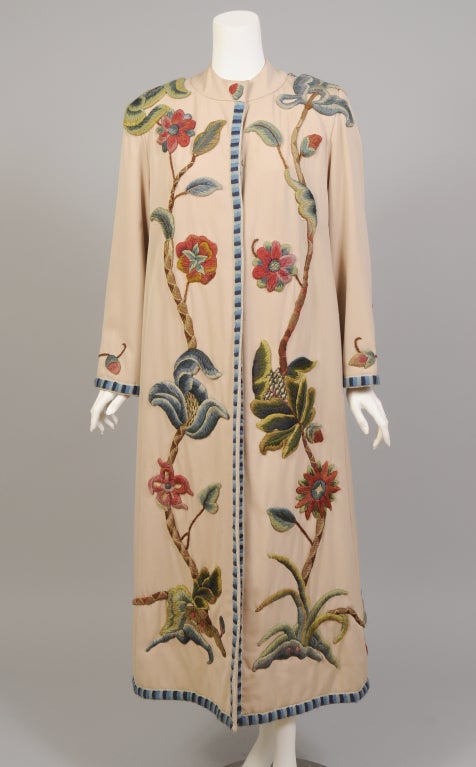 Antique crewel embroidery has been hand appliqued to this custom made wool coat from an Oyster Bay estate. The coat has a band collar, hook and eye closure, two pockets concealed in the side seams, and a matching belt. The applique is beautifully