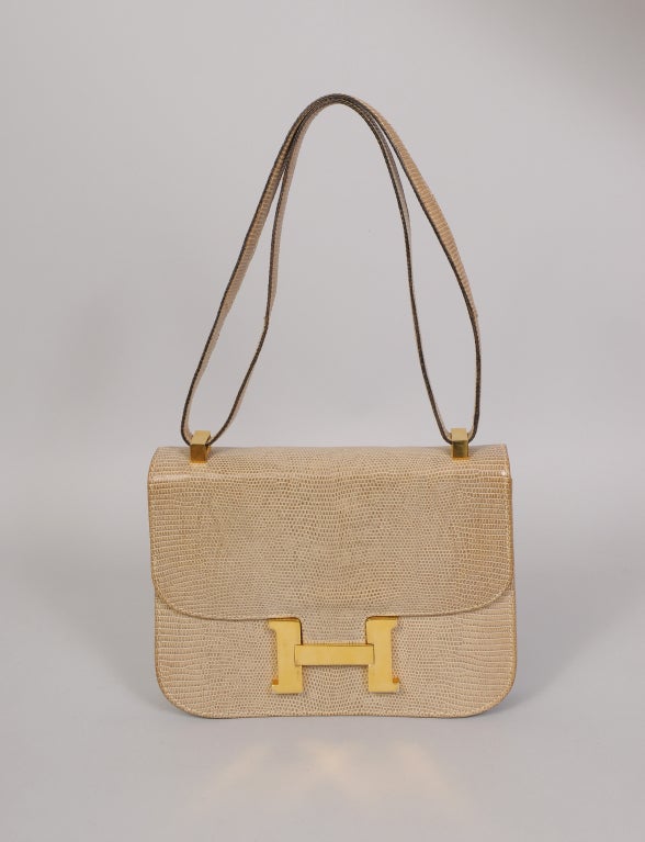 Supple beige lizard skin is accented by gold toned hardware in this day bag with a convertible strap. The bag is fully lined with beige leather. There are two slip pockets and one zippered compartment as well as an open pocket on the back of the