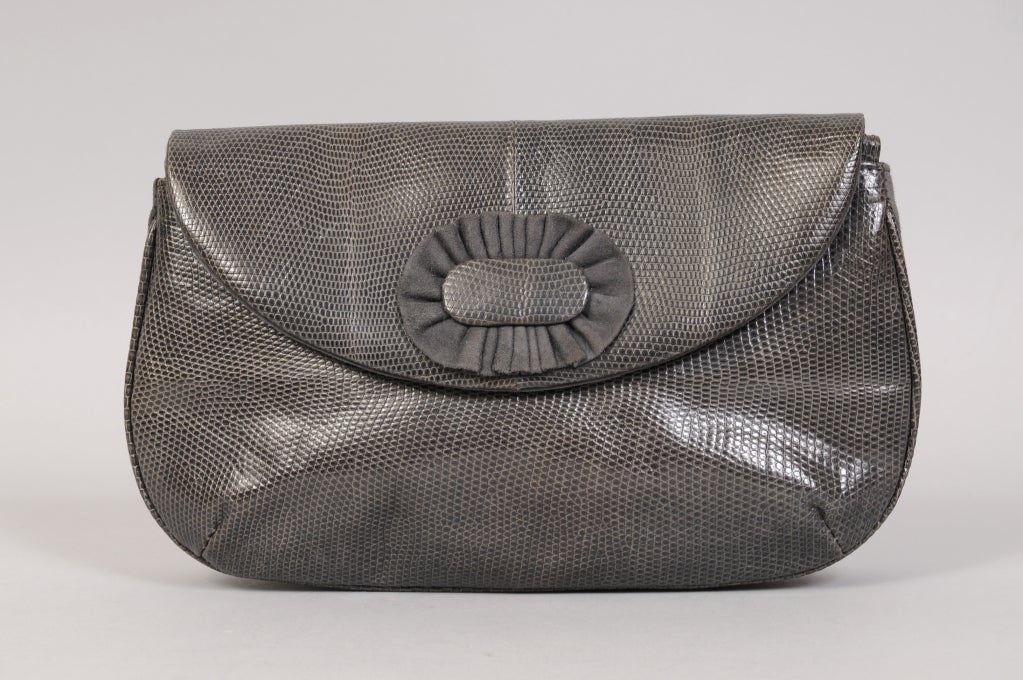 Rich charcoal grey lizard skin is combined with matching grey suede in this chic clutch from Bottega Veneta. The bag is suede and leather lined, with an interior zippered pocket. The original mirror and paperwork are still inside. This bag has never