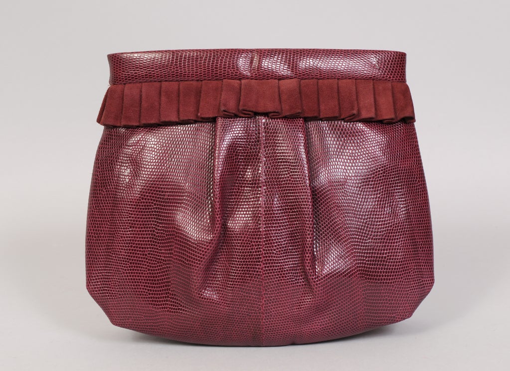Deep carmine red lizard skin is accented with a pleated suede band in this roomy clutch from Bottega Veneta. The leather lined bag has a snap closure, a zippered pocket and a removeable lizard strap. It appears to be unused and is in excellent