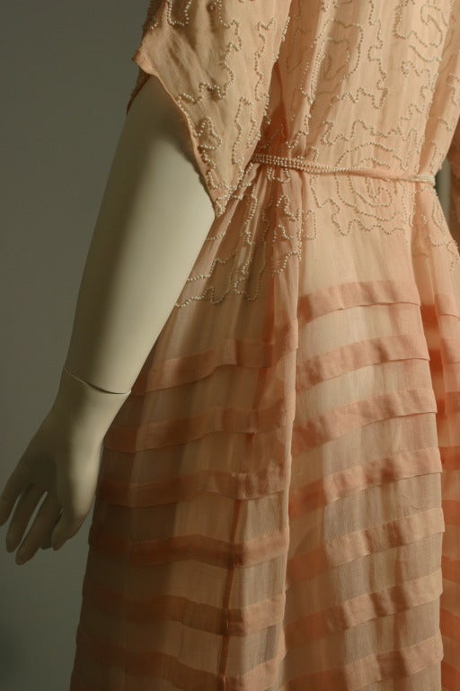 Anonymous, circa 1910-20

A beaded muslin dress, 1910s, the pale pink ground embroidered overall with white beaded scrolls to the hips.
Thin beaded belt ties to the waist.
Band forming pleats from the hips to the hem.
Batwing sleeves with cut