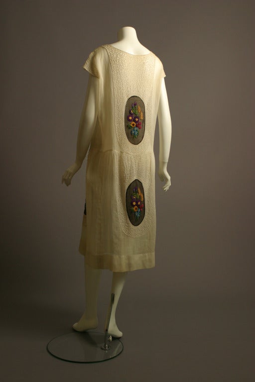 Anonymous, haute couture, circa 1920- 30

Masterly crafted ivory linen batiste dress. Adorned front and back with five oval cameo like inserts of dark batiste hand embroidered chenille work, in an arrangement of colorful flowers
Swags of ivory