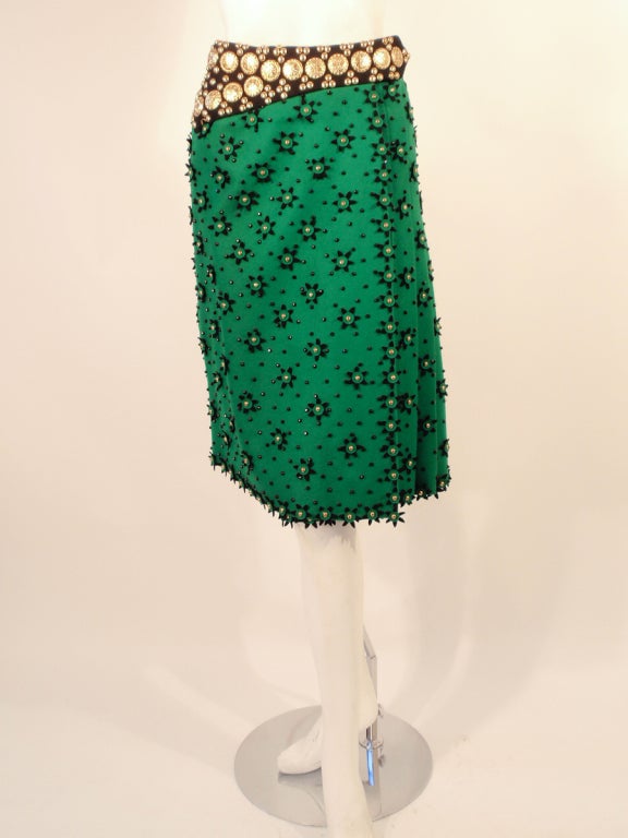 This is a vintage Skirt from Adolfo and it is highly collectible. It is made of a Kelley green heavy felt with black felt flowers. The waist band has gold tome metal coins and studs affixed to it, as well as metal studs on the flowers. It is a wrap