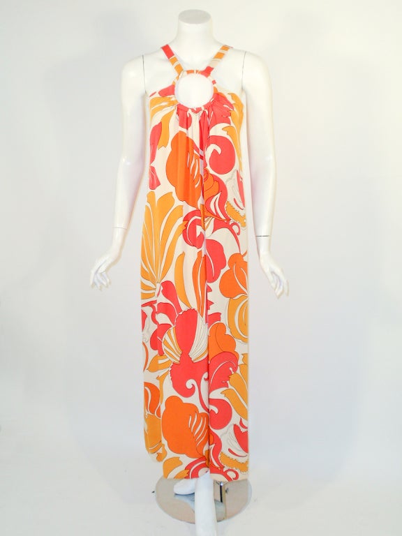 This is a custom made long dress from the 1960's. Attributed to Burke-Amey.
It is made of a brightly printed pink and orange on cream crepe fabric, with the straps and dress attached to a ring on the front of the dress. Side zipper, silk lining.