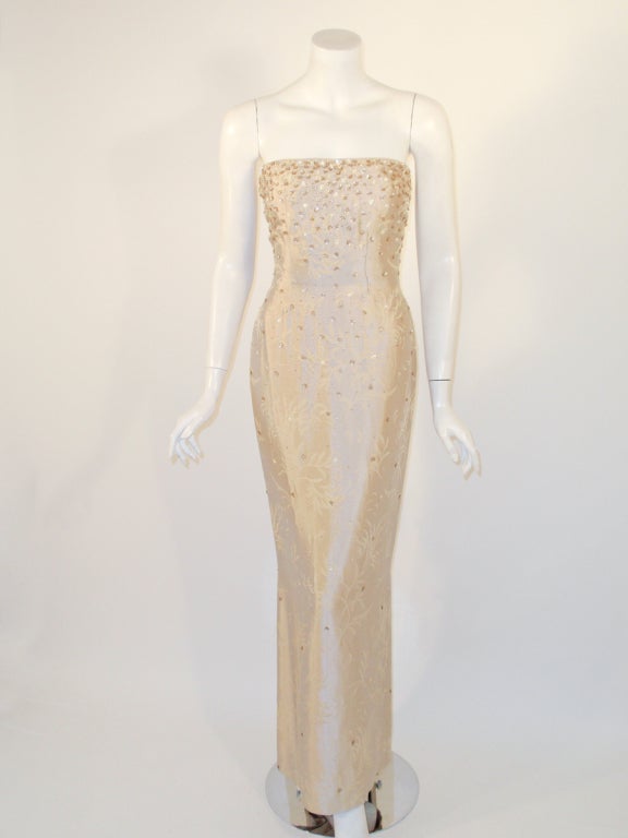 This is a lovely strapless evening gown from Oscar de la Renta. It is made of a beige/ champagne colored silk shantung brocade, with beading and sequin flowers cascading down the entire gown.
The back zipper is off to the side and there is little