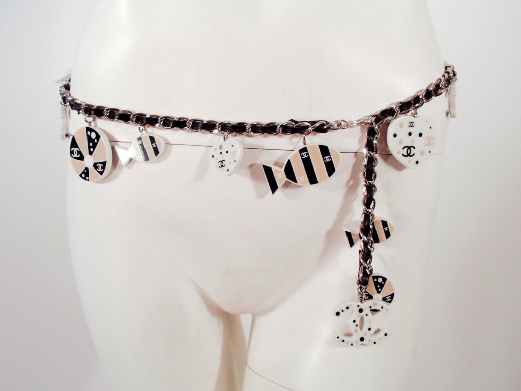 This is a versatile belt from Chanel. It can also be worn as a necklace. Made from a stainless steel chain laced with black leather and charms dangling off of it. The charms are plastic fish, circles, hearts and 