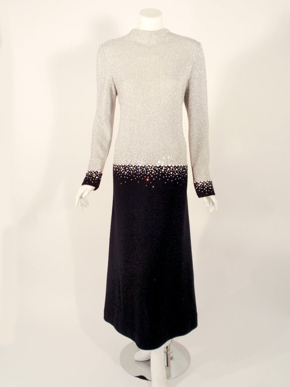This is a stunning evening Gamow from Pauline Trigere. It is made of a silver lurex and black knit and has a fade of big rhinestones at the waistline and the cuffs. The design details are as follows: drop waist, high neck, sheath