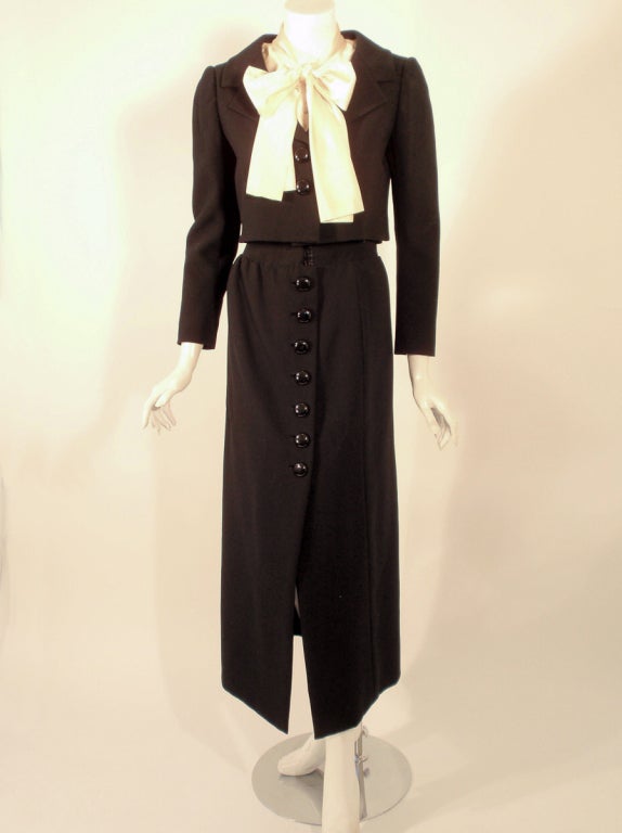 This is a very smart looking vintage 3 piece suit from Norman Norell. It consists of a black cropped jacket and a longer straight skirt that buttons up the front. The sleeveless blouse is made of a silky cream fabric, buttons up the front and has a